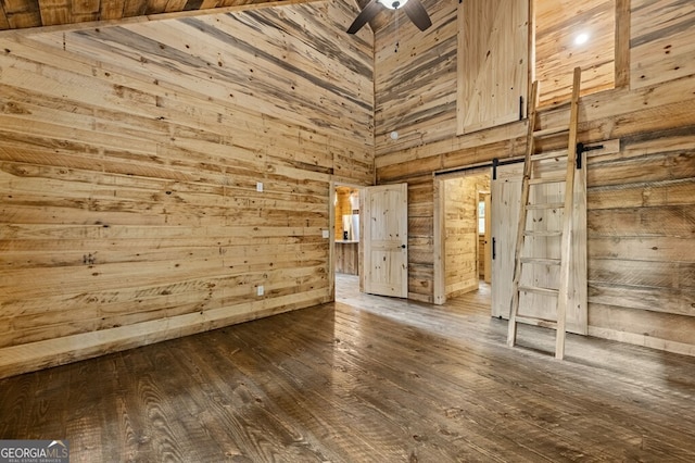 unfurnished room featuring dark hardwood / wood-style flooring, wood walls, ceiling fan, and a barn door