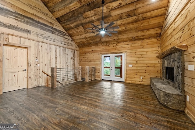 unfurnished living room featuring dark wood-type flooring, wood walls, a fireplace, ceiling fan, and french doors