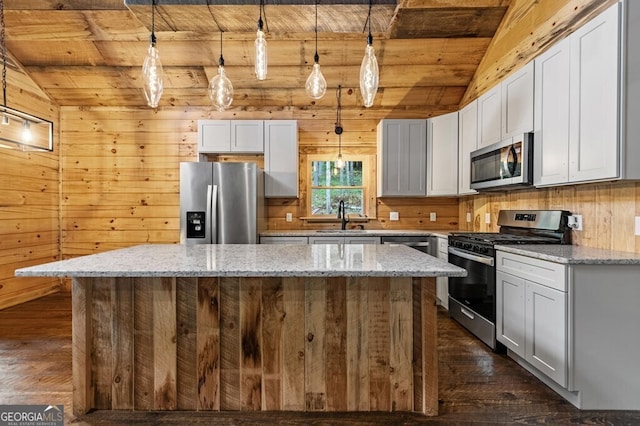 kitchen with appliances with stainless steel finishes, lofted ceiling with beams, light stone countertops, a center island, and decorative light fixtures