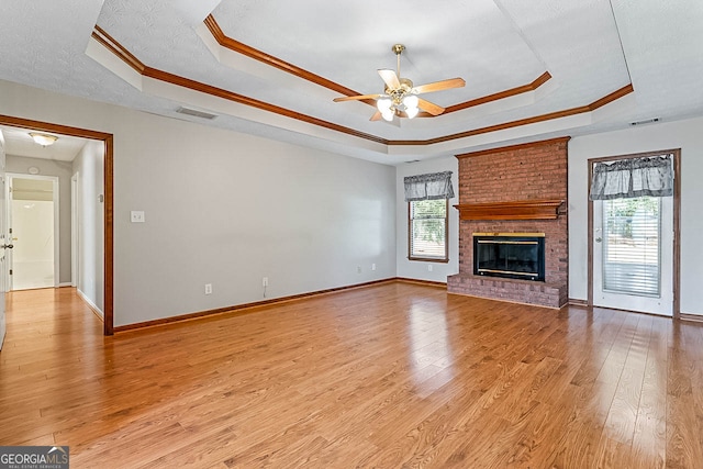 unfurnished living room with light wood-type flooring, a raised ceiling, and plenty of natural light