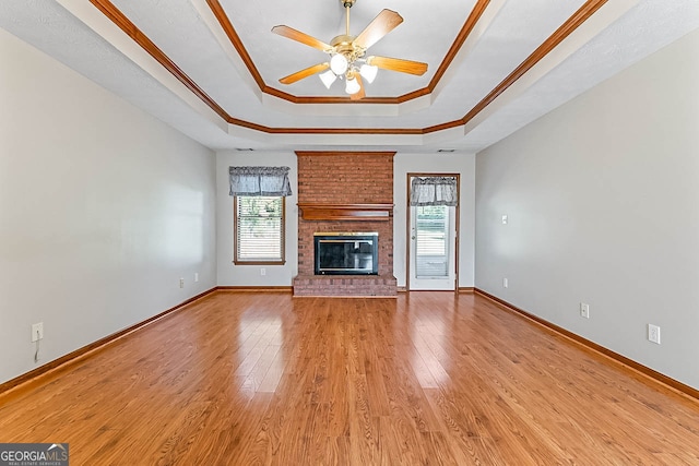 unfurnished living room featuring a fireplace, light wood-type flooring, crown molding, a tray ceiling, and ceiling fan