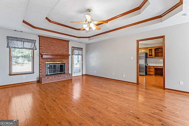 unfurnished living room featuring light hardwood / wood-style floors, a tray ceiling, ceiling fan, and plenty of natural light