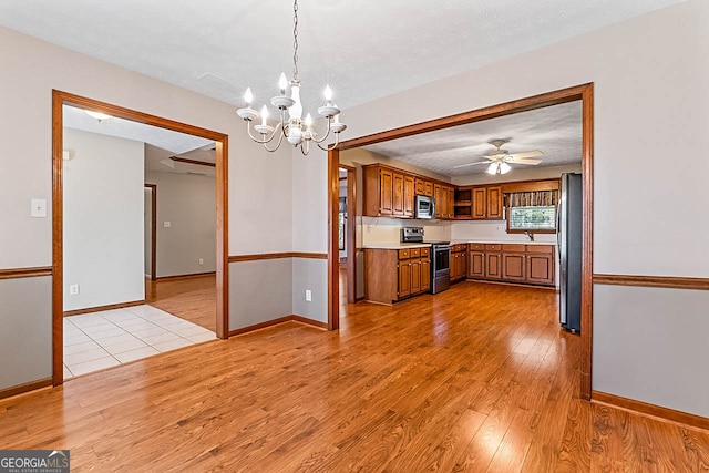 kitchen featuring hanging light fixtures, a textured ceiling, stainless steel appliances, ceiling fan with notable chandelier, and light hardwood / wood-style floors