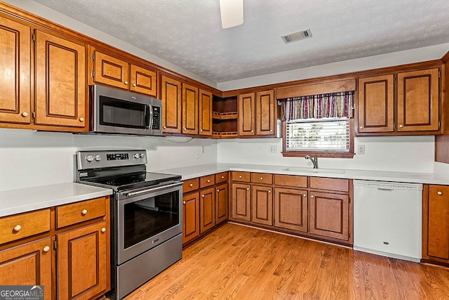 kitchen featuring a textured ceiling, stainless steel appliances, light wood-type flooring, and sink