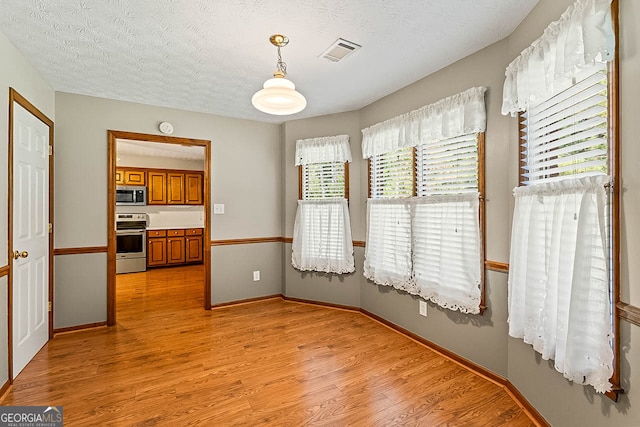 unfurnished dining area featuring light hardwood / wood-style floors and a textured ceiling