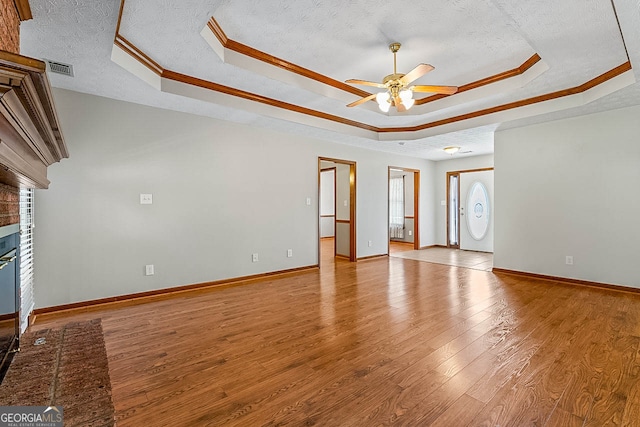 unfurnished living room with light hardwood / wood-style floors, a brick fireplace, a raised ceiling, crown molding, and ceiling fan