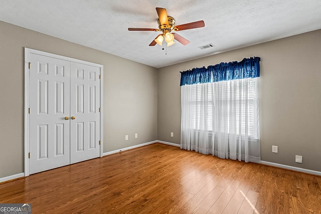 unfurnished bedroom featuring a closet, ceiling fan, hardwood / wood-style floors, and a textured ceiling