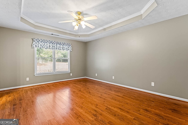 empty room featuring wood-type flooring, a tray ceiling, a textured ceiling, ornamental molding, and ceiling fan