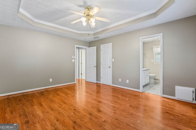 unfurnished bedroom with light hardwood / wood-style flooring, connected bathroom, and a raised ceiling