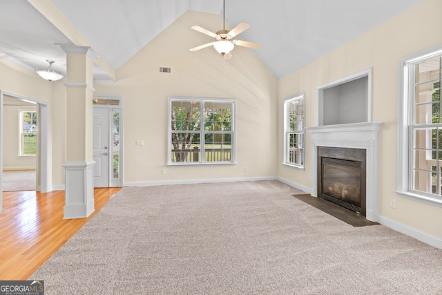 unfurnished living room featuring ceiling fan, high vaulted ceiling, decorative columns, a fireplace, and light hardwood / wood-style floors