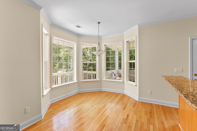 unfurnished dining area featuring light wood-type flooring, crown molding, and a chandelier