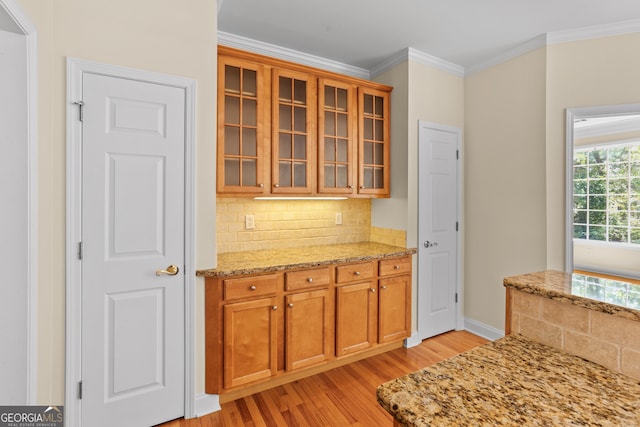 kitchen featuring light stone countertops, light wood-type flooring, ornamental molding, and tasteful backsplash