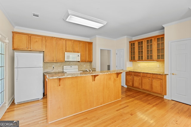 kitchen with light hardwood / wood-style floors, light stone counters, a breakfast bar, white appliances, and crown molding