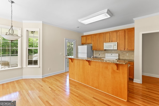 kitchen with light hardwood / wood-style floors, a healthy amount of sunlight, white appliances, and hanging light fixtures