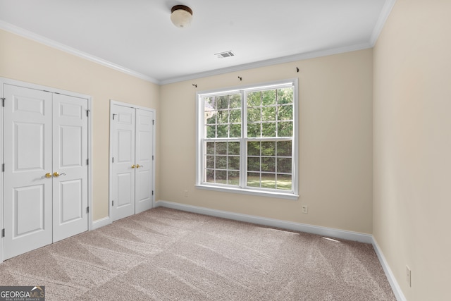 unfurnished bedroom featuring carpet, multiple closets, and crown molding