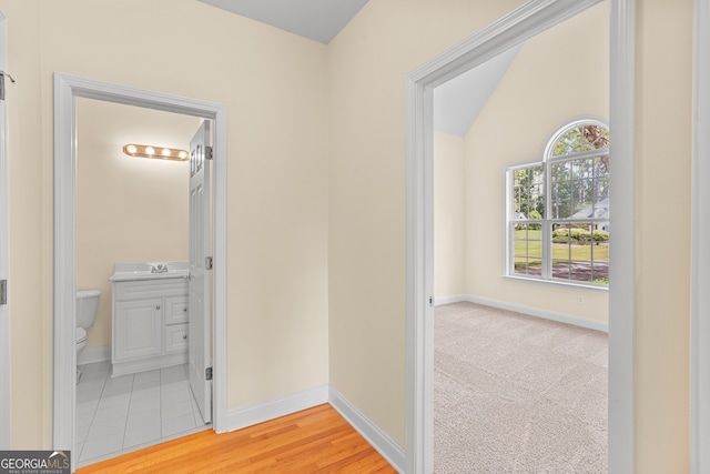 hallway with vaulted ceiling, light hardwood / wood-style floors, and sink