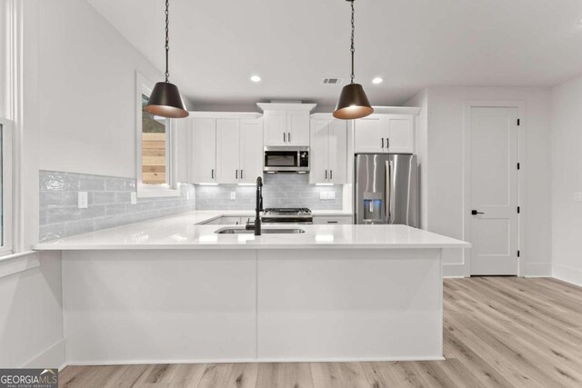 kitchen with pendant lighting, appliances with stainless steel finishes, white cabinets, and light hardwood / wood-style flooring
