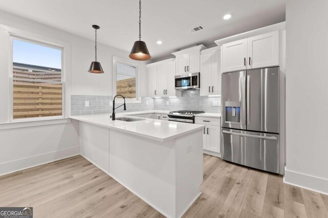 kitchen with white cabinets, pendant lighting, stainless steel appliances, light wood-type flooring, and sink
