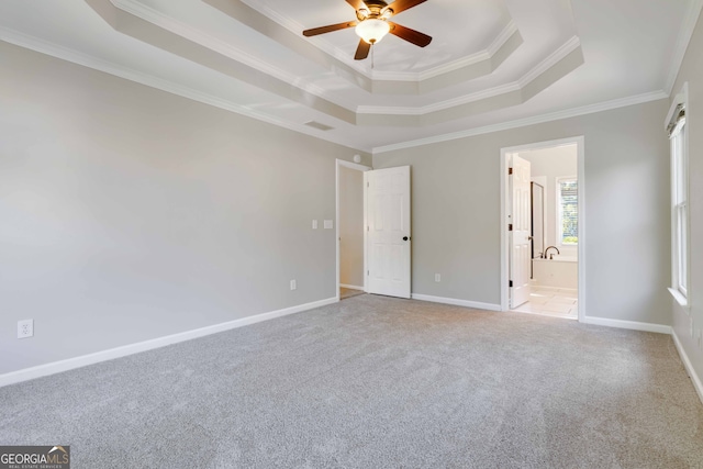 interior space with a tray ceiling, ceiling fan, carpet, ornamental molding, and ensuite bath