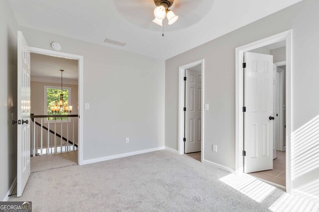 unfurnished bedroom featuring ceiling fan with notable chandelier and light carpet