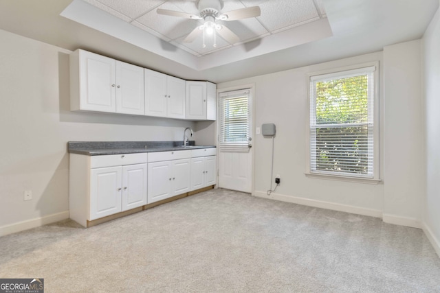 kitchen featuring light carpet, white cabinetry, ceiling fan, and a raised ceiling