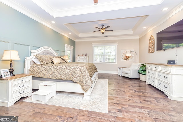 bedroom featuring hardwood / wood-style flooring, crown molding, ceiling fan, and a tray ceiling