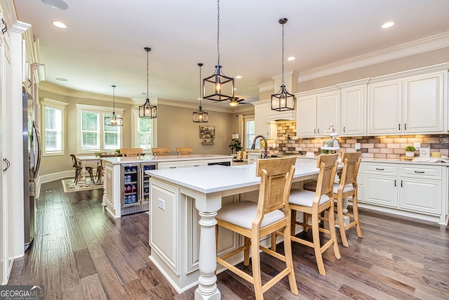 kitchen featuring a kitchen island with sink, crown molding, a breakfast bar, dark wood-type flooring, and white cabinetry