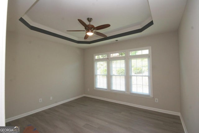 unfurnished room with ornamental molding, ceiling fan, dark wood-type flooring, and a raised ceiling