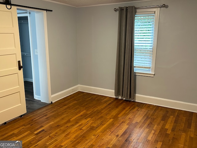 empty room with a barn door, ornamental molding, and dark hardwood / wood-style floors