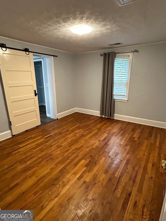 unfurnished bedroom featuring a textured ceiling, a barn door, and hardwood / wood-style floors