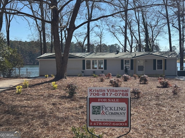 single story home featuring metal roof, a water view, and fence