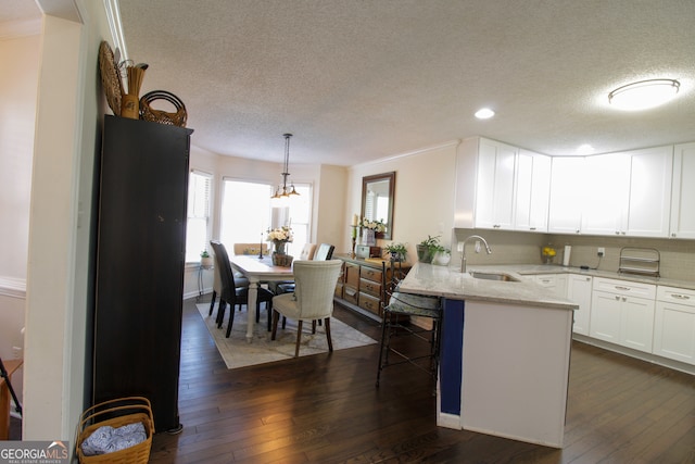 kitchen featuring pendant lighting, sink, white cabinets, kitchen peninsula, and dark hardwood / wood-style flooring