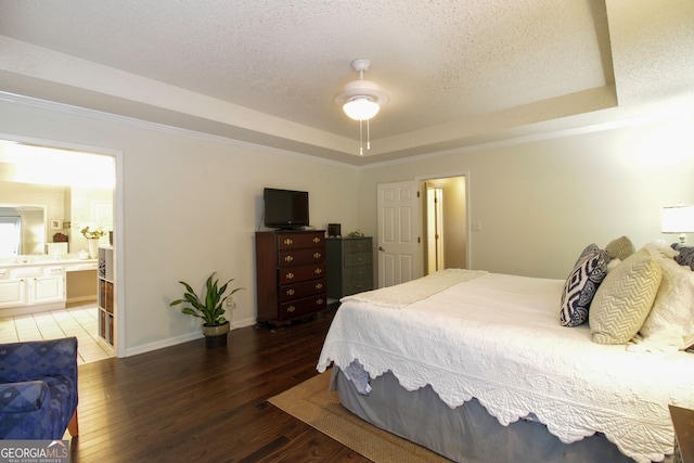 bedroom featuring dark wood-type flooring, a raised ceiling, connected bathroom, a textured ceiling, and ceiling fan