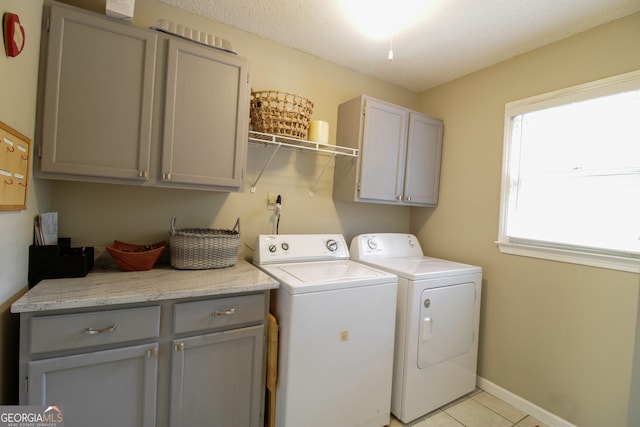 laundry area featuring a textured ceiling, separate washer and dryer, light tile patterned floors, and cabinets