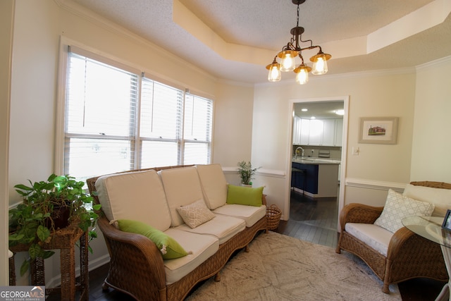 living room featuring crown molding, a raised ceiling, hardwood / wood-style floors, and a notable chandelier