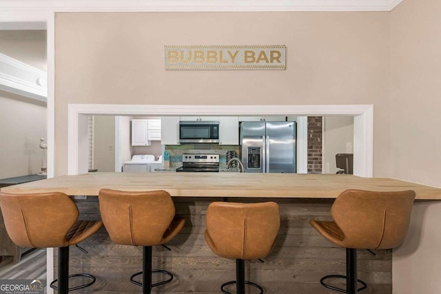 bar featuring sink, white cabinetry, stainless steel appliances, separate washer and dryer, and crown molding