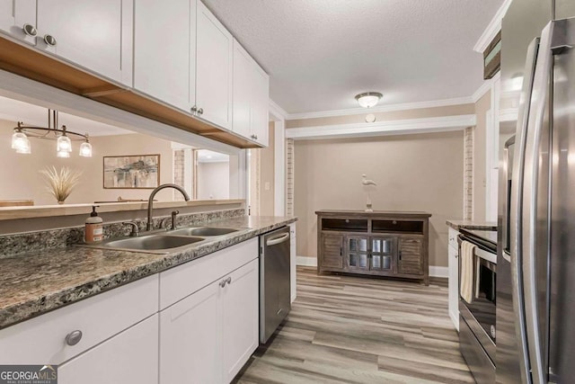 kitchen featuring white cabinets, ornamental molding, sink, appliances with stainless steel finishes, and light wood-type flooring