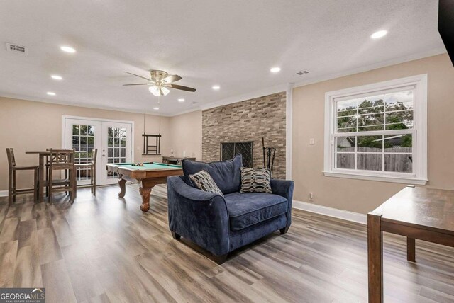 living room with a healthy amount of sunlight, pool table, french doors, and a stone fireplace