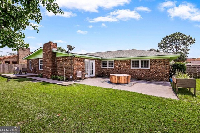 rear view of house featuring a wooden deck, a lawn, a patio, and a hot tub