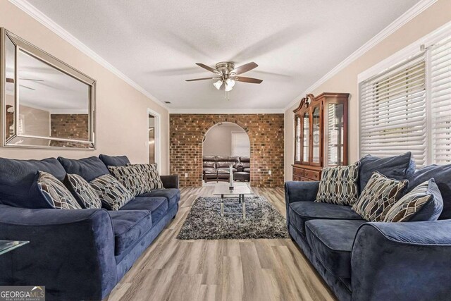 living room with brick wall, a textured ceiling, crown molding, ceiling fan, and hardwood / wood-style flooring