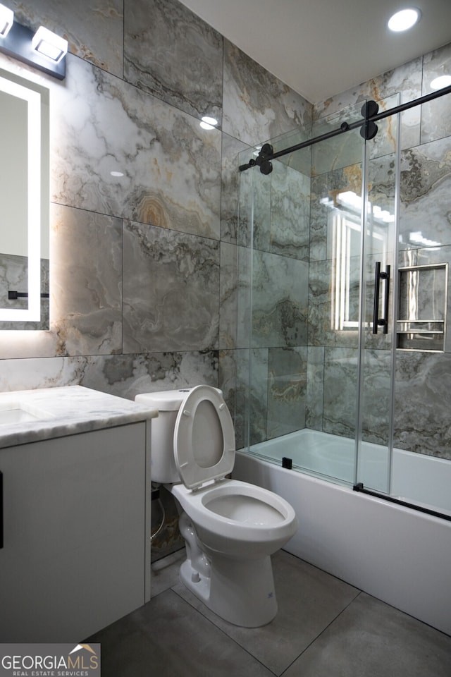 full bathroom featuring tile walls, tile patterned floors, bath / shower combo with glass door, vanity, and toilet