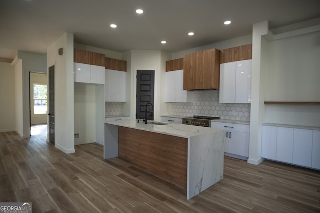 kitchen with an island with sink, sink, hardwood / wood-style flooring, and white cabinetry