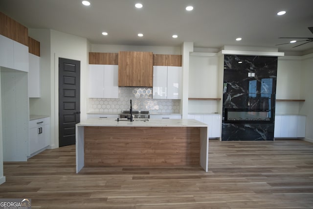 kitchen featuring decorative backsplash, a kitchen island with sink, hardwood / wood-style floors, and white cabinets