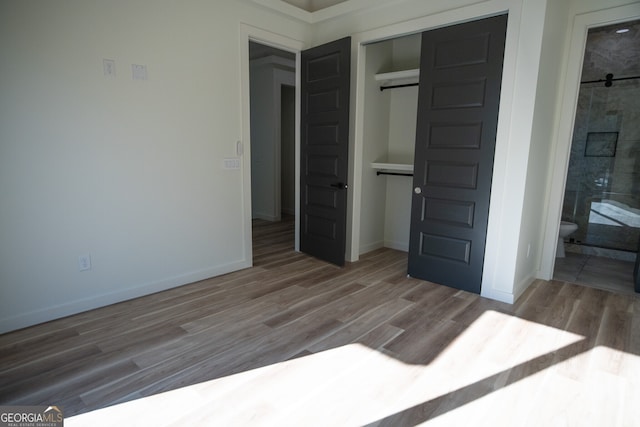 unfurnished bedroom with a barn door, hardwood / wood-style floors, ensuite bathroom, and a closet