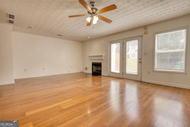 unfurnished living room with ceiling fan, a textured ceiling, and light hardwood / wood-style flooring