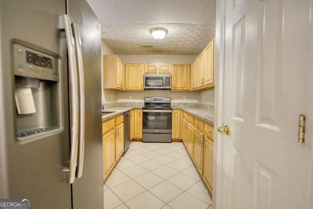 kitchen with light stone counters, a textured ceiling, stainless steel appliances, light tile patterned floors, and light brown cabinetry