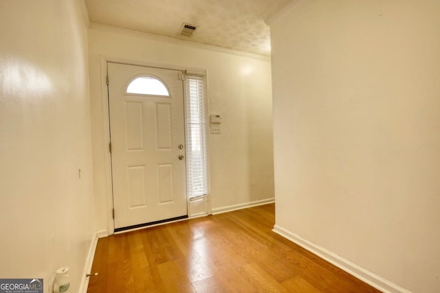 entrance foyer featuring a textured ceiling, ornamental molding, and light hardwood / wood-style flooring