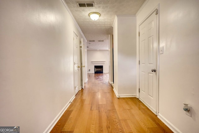 hall with light hardwood / wood-style flooring, a textured ceiling, and crown molding