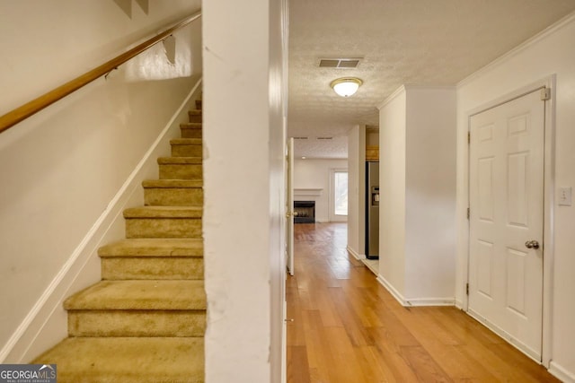 stairs with a textured ceiling, ornamental molding, and hardwood / wood-style floors