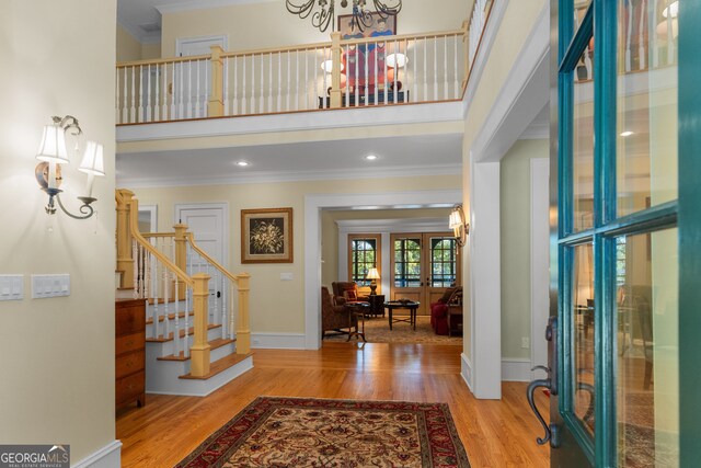 entryway with ornamental molding, a high ceiling, a notable chandelier, and hardwood / wood-style flooring